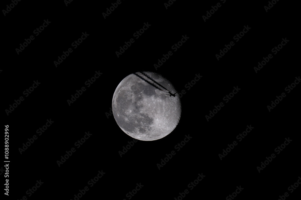 Obraz premium The moon in the night sky with a silhouette of an airplane. The moon in the dark sky with a plane flying over it.