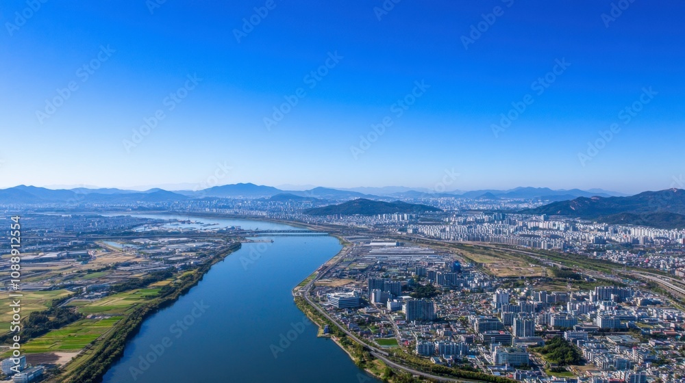 Breathtaking Aerial View Over a Serene River Flowing Through Lush Green Landscapes and Urban Developments Under a Clear Blue Sky Breathtaking Aerial View Over a Serene River Flowing Through Lush Green Landscapes and Urban Developments Under a Clear Blue Sky