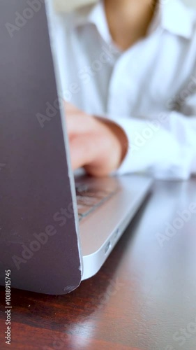 テーブルの上でノートパソコンをタイピングする若い女性・白いシャツ・縦長・ビデオ