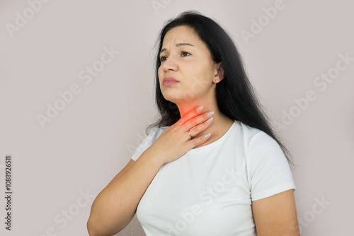 Unhappy young brunette with closed eyes suffering from sore throat touching red inflamed area on neck, studio background series photo