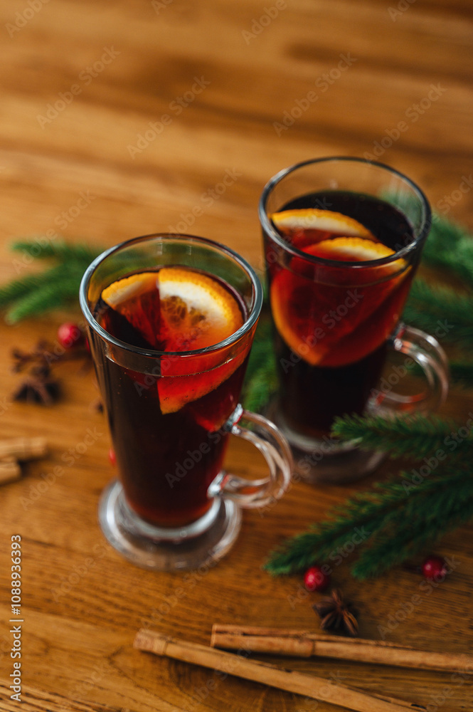 Two glasses of christmas mulled wine with oranges and spices on wooden background