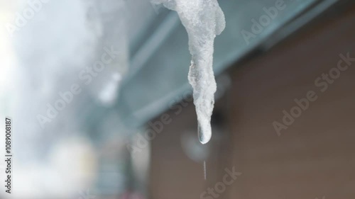 An icicle slowly melting and dripping from a rooftop, capturing the essence of a winter thaw in 4K slow motion 60fps