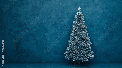 Snowy Christmas tree against a blue wall backdrop.
