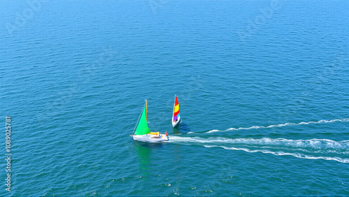 A race of colorful sailboats on the open sea, with one boat leading and others in line behind it photo