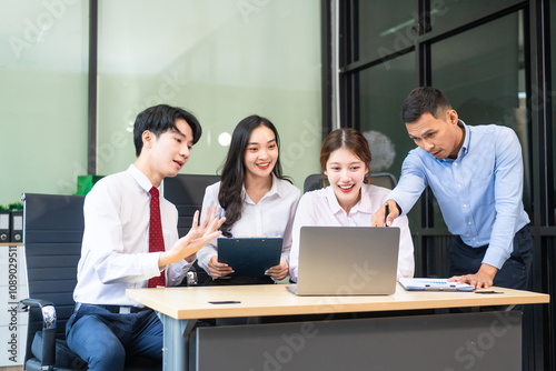 Two young businessmen and two beautiful women sit at a desk in the office, talking, working, watching computers, exchanging gifts, and laughing joyfully while celebrating welcoming Happy New Year