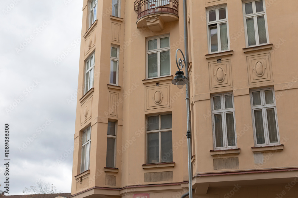 Fototapeta premium An elegant yellow apartment building stands as a stunning example of unique architecture, beautifully incorporating urban elements such as a charming balcony and a decorative street lamp