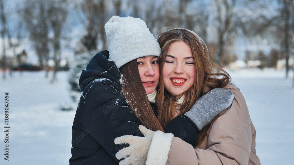Two joyful schoolgirls hugging in a snowy park, savoring their winter fun together