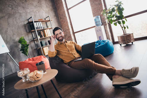 Full size photo of nice young male sit beanbag netbook wear yellow shirt formalwear coworking successful businessman nice light office photo