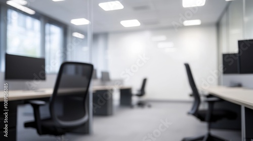 A modern office space with multiple workstations, featuring computer monitors and ergonomic chairs, all set in a bright, minimalistic environment.