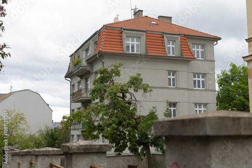 This historic multiunit residential building boasts a vibrant red roof, surrounded by lush greenery in an urban area, providing a tranquil sanctuary and peaceful refuge for residents