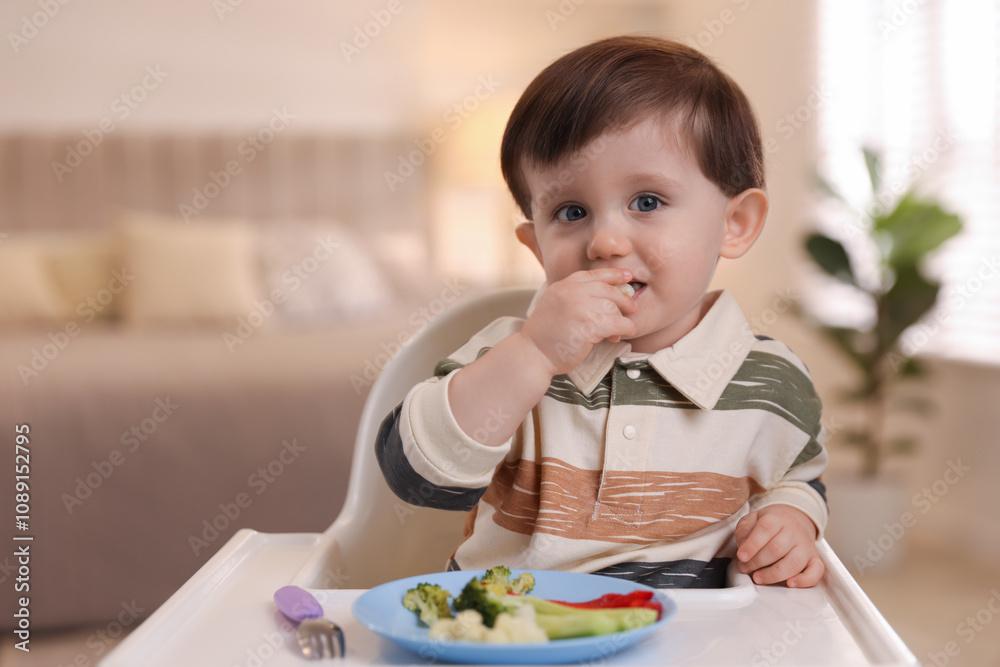 Cute little baby eating healthy food in high chair at home Cute little baby eating healthy food in high chair at home