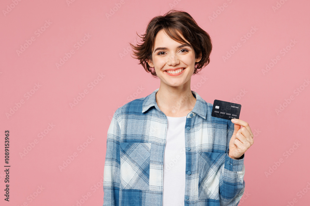 Young cheerful happy woman she wear blue shirt white t-shirt casual clothes hold in hand mock up of credit bank card isolated on plain pastel light pink background studio portrait. Lifestyle concept. Young cheerful happy woman she wear blue shirt white t-shirt casual clothes hold in hand mock up of credit bank card isolated on plain pastel light pink background studio portrait. Lifestyle concept.
