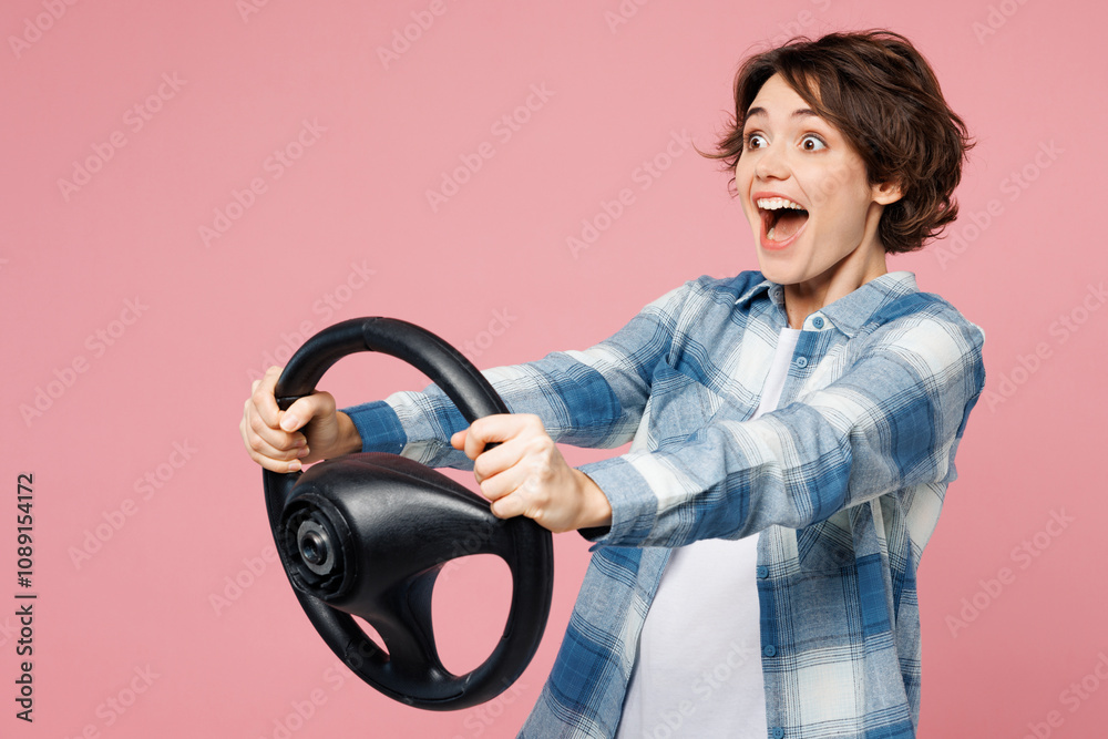 Side view young excited surprised shocked woman wear blue shirt white t-shirt casual clothes hold steering wheel driving car isolated on plain pastel light pink background studio. Lifestyle concept. Side view young excited surprised shocked woman wear blue shirt white t-shirt casual clothes hold steering wheel driving car isolated on plain pastel light pink background studio. Lifestyle concept.
