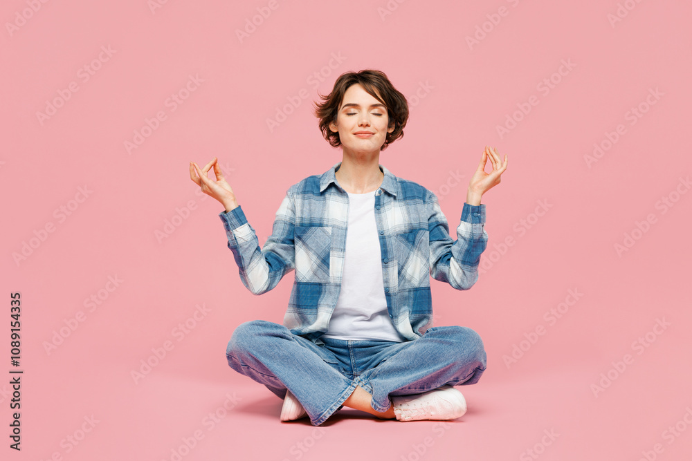 Full body young woman wear blue shirt white t-shirt casual clothes sits hold hands in yoga om aum gesture relax meditate try to calm down isolated on plain pastel pink background. Lifestyle concept. Full body young woman wear blue shirt white t-shirt casual clothes sits hold hands in yoga om aum gesture relax meditate try to calm down isolated on plain pastel pink background. Lifestyle concept.
