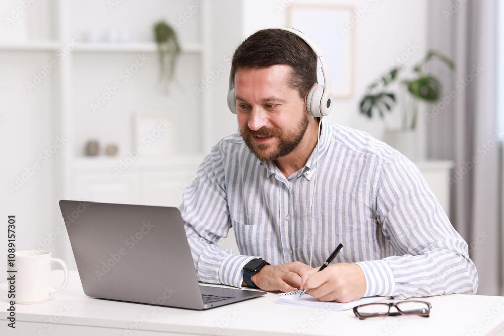 Interpreter in headphones taking notes while having video chat via laptop at white table indoors Interpreter in headphones taking notes while having video chat via laptop at white table indoors