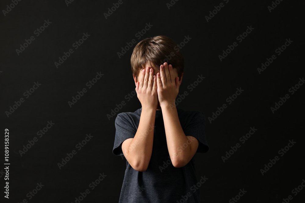 Scared little boy covering face with hands on black background Scared little boy covering face with hands on black background