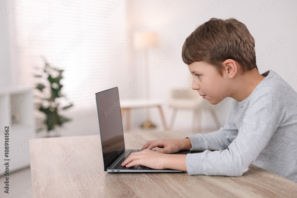 Boy with incorrect posture using laptop at wooden desk indoors Boy with incorrect posture using laptop at wooden desk indoors