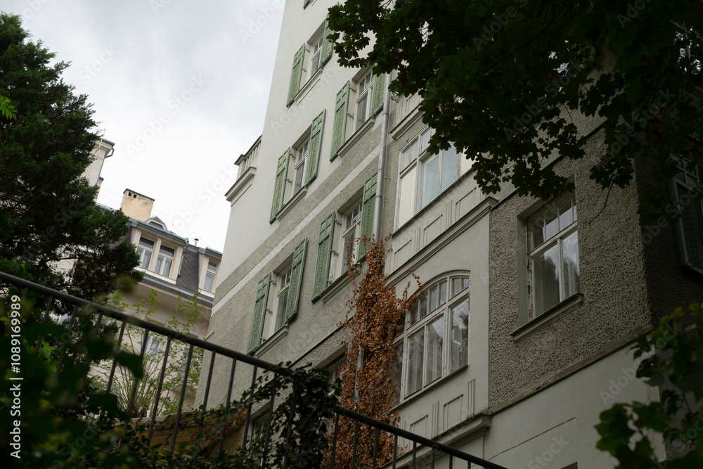 A beautifully designed urban building with decorative green shutters and lush ivy climbing up its walls, set against a serene backdrop of a cloudy sky within a charming city environment A beautifully designed urban building with decorative green shutters and lush ivy climbing up its walls, set against a serene backdrop of a cloudy sky within a charming city environment