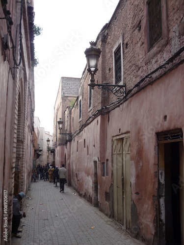  narrow, winding alley in the heart of the Moroccan medina, lined with weathered stone buildings and adorned with wrought iron lanterns.