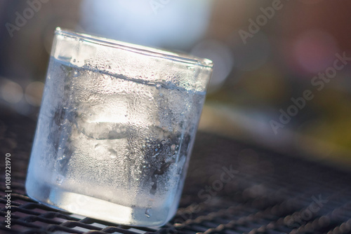 clear glass filled with ice and water. The glass is placed on a metal grid surface, and there is condensation on the outside of the glass, indicating that the contents are cold. photo