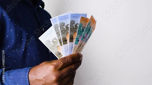  Black African male man wearing blue long sleaves shirt holding and waving Zimbabwean gold zig notes against white backgound with copy space photo