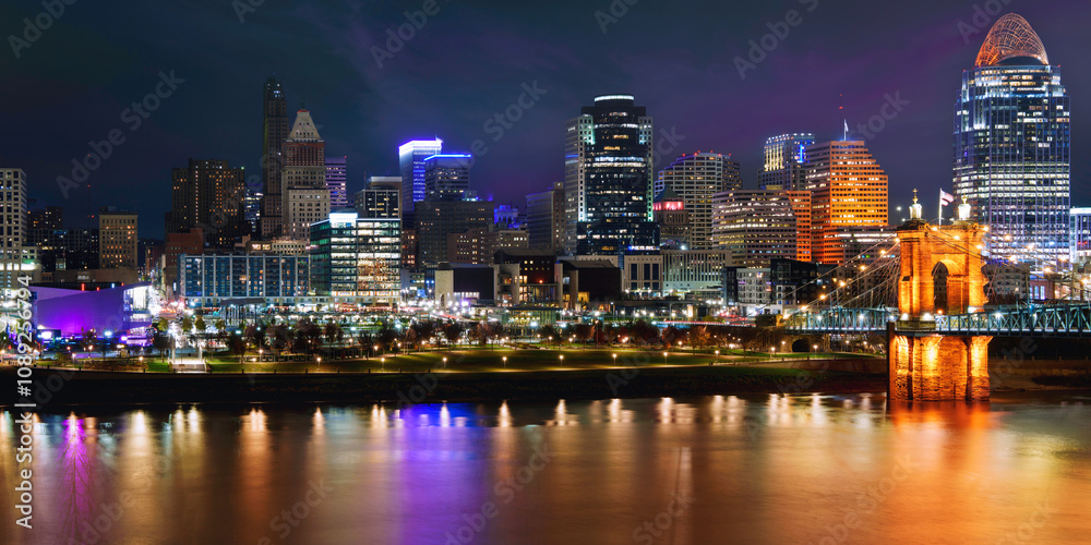 Fototapeta premium Cincinnati City Skyline Nightscape over the Ohio River, Lighted Riverside Park, and Roebling Suspension Bridge reflected on the water in Kentucky, USA