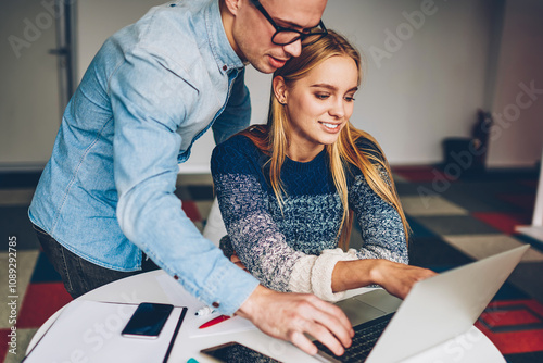 Young female employee pointing on laptop computer monitor watching video with male colleague creating project,coworkers reading financial news on netbook making business plan together in office