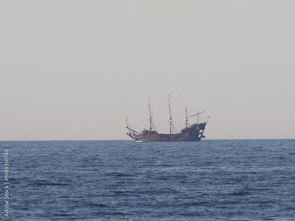 Antique sailing ship on the horizon in calm sea under clear sky