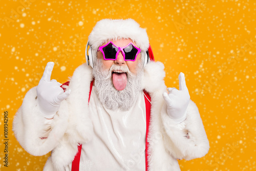 Close up photo of crazy funny hipster santa claus show horns sign tongue-out want rock-and-roll concert instead x-mas tradition celebration wear hat trendy suspenders isolated yellow color background photo