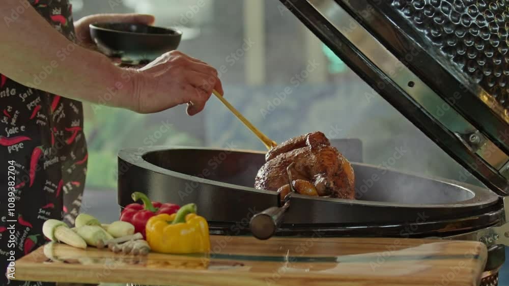 hand brushing roasted whole chicken on a the grill bbq barbeque kamado camado	