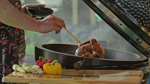 hand brushing roasted whole chicken on a the grill bbq barbeque kamado camado	