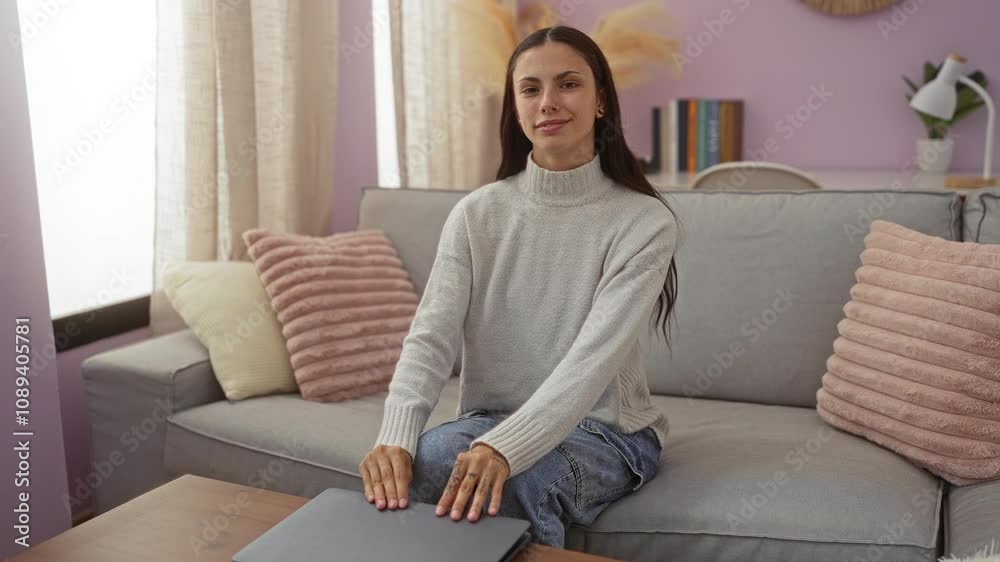 Young woman closing laptop sitting on couch in cozy living room, surrounded by pink pillows and bookshelves, exuding a calm and relaxed atmosphere Young woman closing laptop sitting on couch in cozy living room, surrounded by pink pillows and bookshelves, exuding a calm and relaxed atmosphere