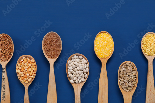 Different types of cereals, seeds and legumes in spoons on blue wooden table, flat lay