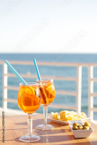 Fototapeta Naklejka Na Ścianę i Meble -  Aperol spritz cocktail glasses with olives and potatoes chips aperitif, very Mediterranean. Sea views, gastronomy and travel concept.