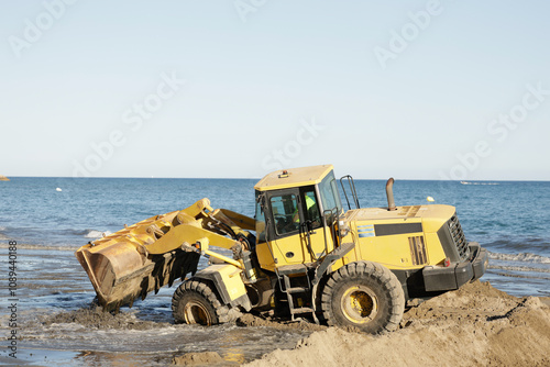 Yellow tractor on the beach, with sand and sea, used to smooth sand and manage erosion problems by replacing lost sand.