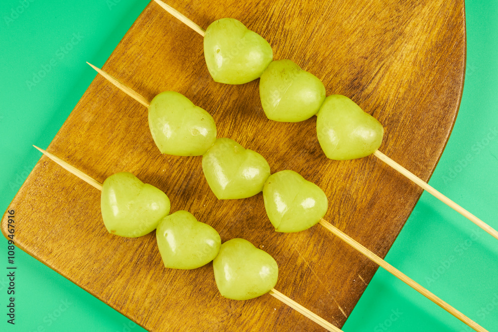 Heart shaped grapes stacked representing a skewer on a wooden board with a green background Heart shaped grapes stacked representing a skewer on a wooden board with a green background