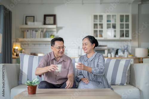 An elderly couple enjoys a peaceful moment at home, sharing smiles and drinks. The warm and cozy atmosphere emphasizes their deep connection, happiness, and the comfort of spending time together.