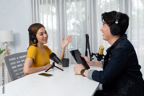 Smiling radio influencer host holding tablet wearing headphones interview woman speaker social media online live streaming channel with talking to share link at morning at studio record. Infobahn.