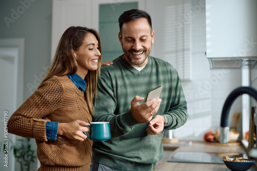 Happy couple using smart phone in kitchen.