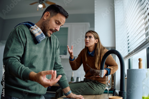 Fotografie Frustrated man arguing with his wife while doing dishes in kitchen