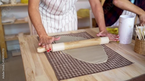Artist rolling out clay on a textured table in pottery studio. 