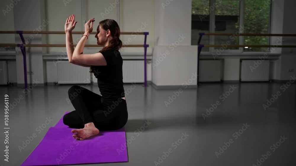 in studio of spiritual development master class on yoga girl with long hair and black tracksuit on purple mat sits with folded arms and legs pose asana in studio of spiritual development master class on yoga girl with long hair and black tracksuit on purple mat sits with folded arms and legs pose asana
