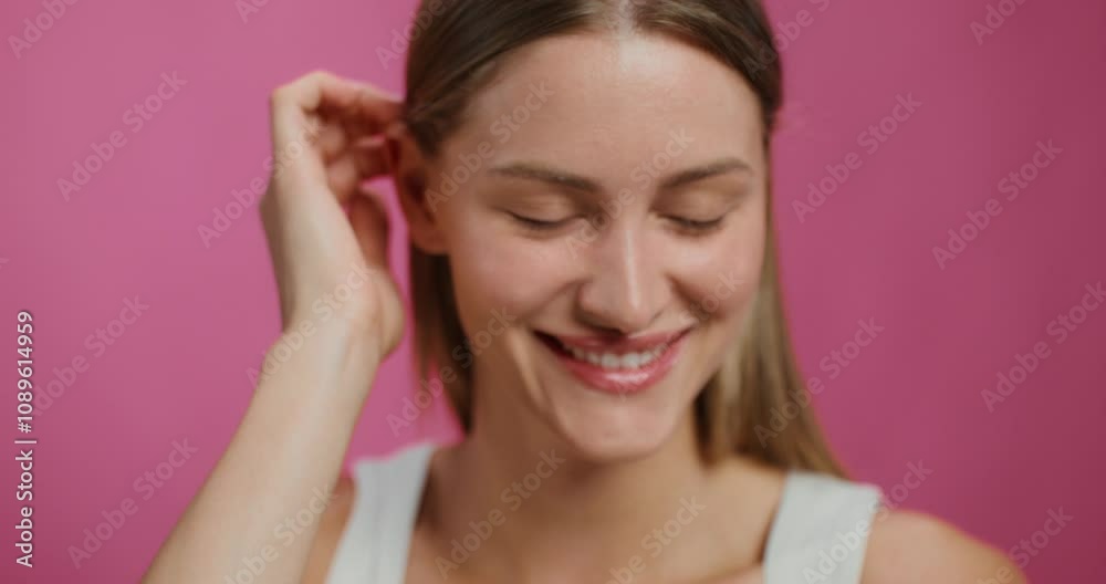 A woman smiles looking at the camera standing on a studio background. She adjusts her hair A woman smiles looking at the camera standing on a studio background. She adjusts her hair