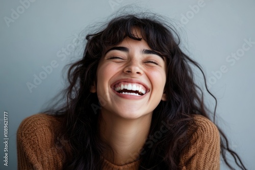 A smiling woman wearing a brown sweater and having long dark hair