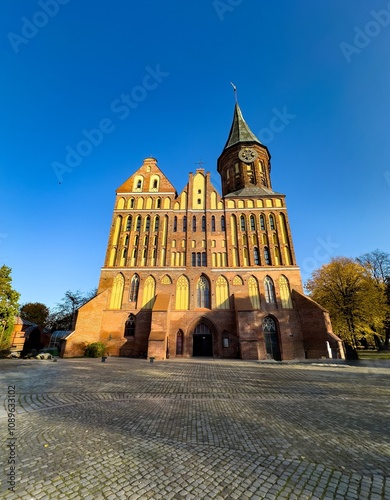 A striking front facing view of the historic Konigsberg Cathedral, showcasing its red brick gothic architecture against a vibrant blue sky. The elegant tower and detailed facade reflect the grandeur photo