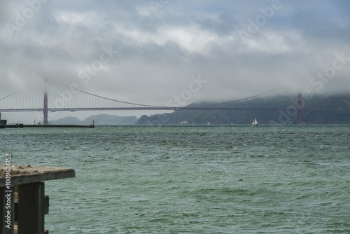 Backlit silhouette of world famous red steel suspension bridge in San Francisco port entrance with Golden Gate State park nature lands hidden in cloud mist fog bank with clear sky pilars photo