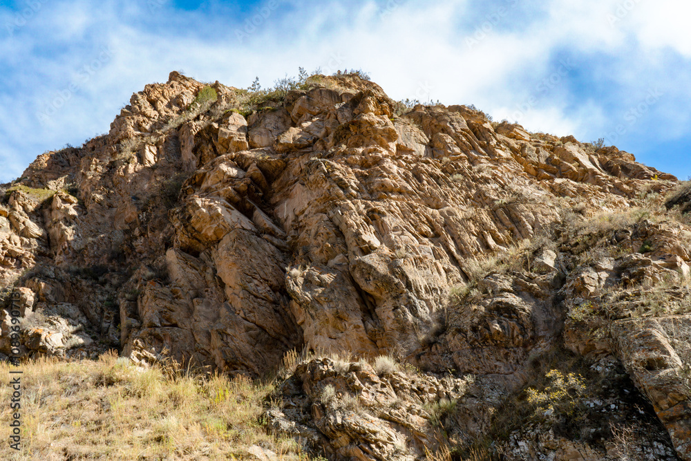 Fototapeta premium A rugged cliffside with exposed rock formations and patches of dry grass under a clear blue sky. A striking natural feature that highlights geological textures and the beauty of untouched landscapes.