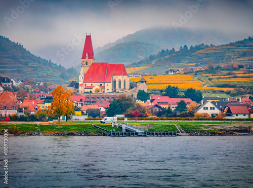 Gloomy autumn view of Weisenkirchen parish church on the shore of Dunabe river. Splendid morning cityscape of Weisenkirchen in der Wachau town, district of Krems-Land in Lower Austria, Europe. photo