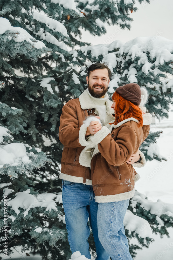 Fototapeta premium Love romantic couple lovestory. Brutal bearded man, bright red-haired girl woman in winter park. Romantic date, kissing, hugging. Walking, having fun. Stylish clothes, red sheepskin coat, jacket, hat