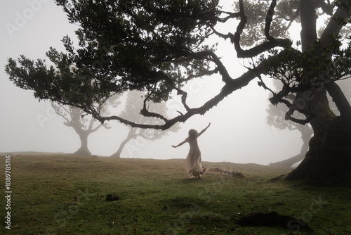 lightfooted girl in long white dress dancing under the trees on a misty morning photo